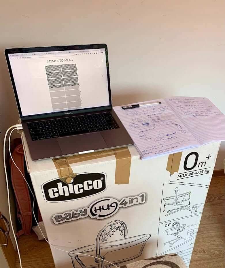 A MacBook and an open notebook balanced on a Chicco crib box, August 2021